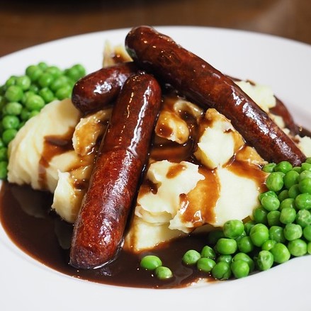 A plate of sausage, mash and peas