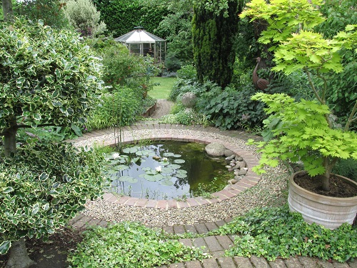 A circular pond with octagonal greenhouse in the background